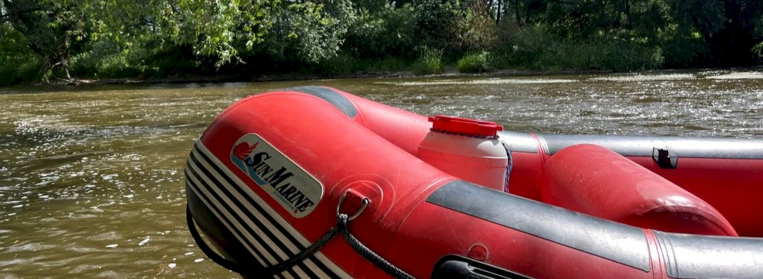 Schlauchbootspitze in rot vor einem Fluss mit Bäumen im Hintergrund